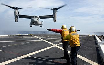 两名机组人员帮助一架军用飞机在海上的一艘船上降落